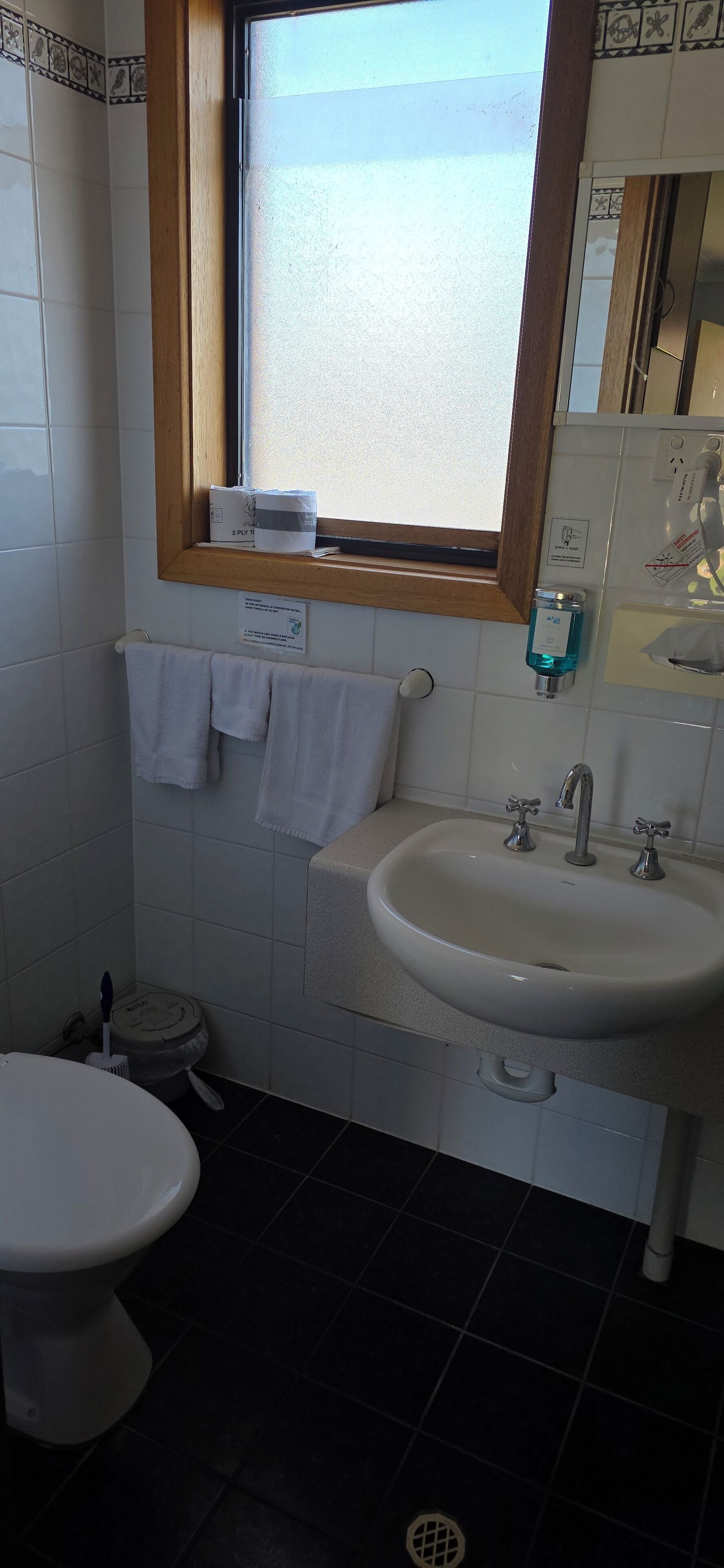 A bathroom with a white sink, a window above the sink, a towel rack with a white towel, and a toilet.