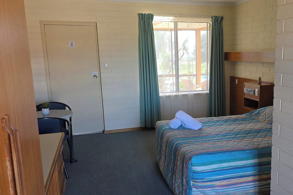 A compact room with a bed, a desk, a chair, and a window with curtains.