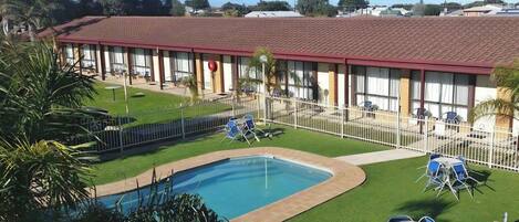 Un hotel con piscina, mobiliario exterior y un patio cercado.