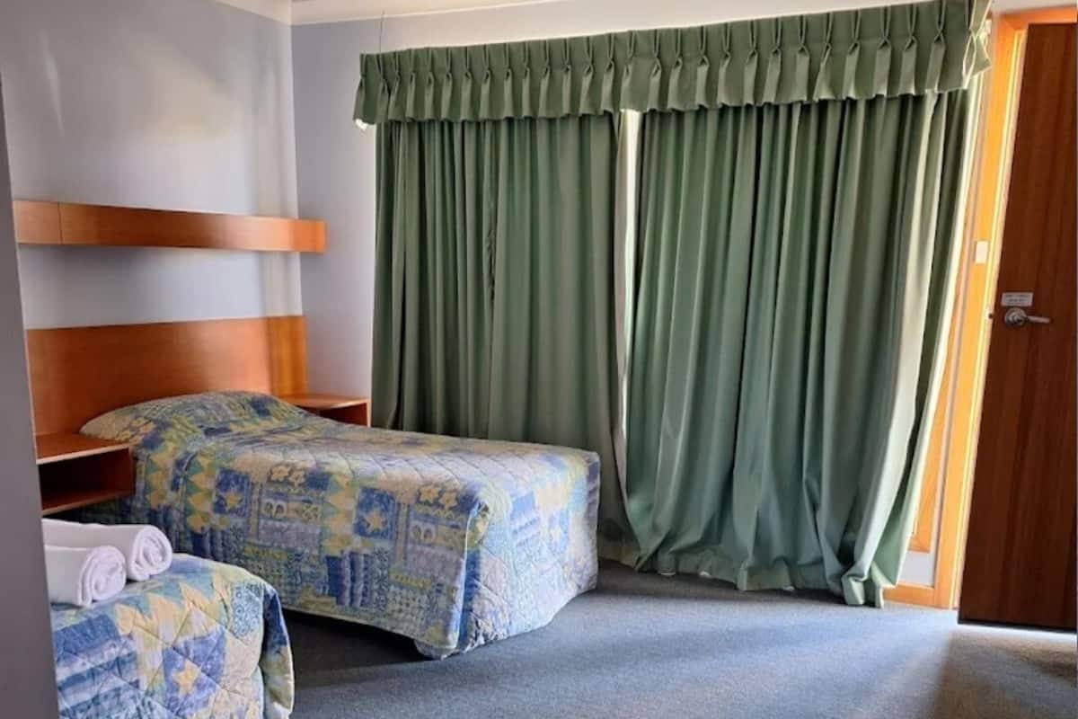 A hotel room with two beds, a wooden headboard, a green curtain, and a carpeted floor.