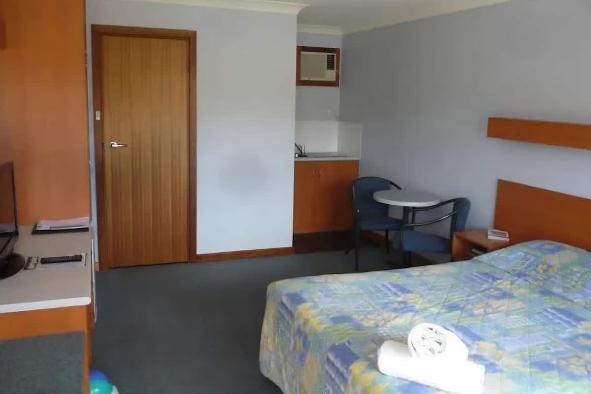 A hotel room with a bed, a desk with a chair, a small kitchenette, and a bathroom.