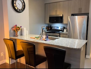 Une cuisine moderne dotée de plans de travail en granit, d’appareils électroménagers en acier inoxydable et de tabourets de bar noirs.