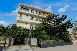 A multi-story residential building with a gated entrance, surrounded by lush greenery and a clear sky.