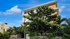 A modern two-story building with a white facade, surrounded by lush greenery and a white picket fence. - Villa Verizon by Dancenter (Hyderabad)