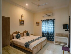 A bedroom with a bed, bedside tables, a ceiling fan, an air conditioner, a TV, and a window with curtains. - Villa Sagat Raaso (Udaipur)