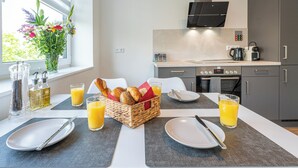 Et moderne køkken med et spisebord dækket til morgenmad, inklusiv tallerkener, bestik og en kurv med brød og kager.