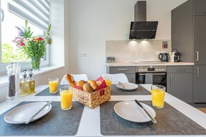 A modern kitchen with a dining table set for breakfast, including plates, cutlery, and a basket of bread and pastries. - Skipper's Deck: Modern, near harbor & dike, incl. parking, 2 workstations, wifi (Bremerhaven)