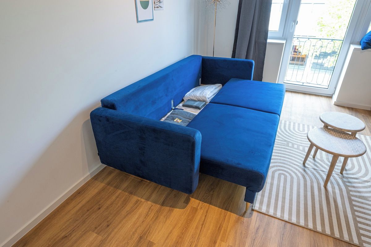 Ein blaues Sofa in einem Raum mit Holzboden, einem kleinen runden Tisch und einem gemusterten Teppich.