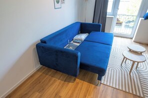 Un canapé bleu dans une pièce dotée d’un plancher en bois, d’une petite table ronde et d’un tapis à motifs.