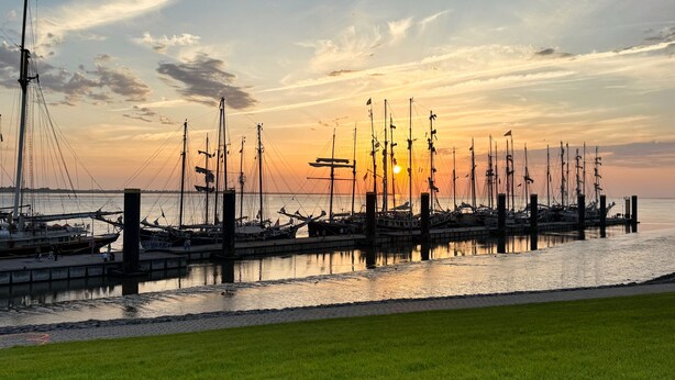 En lystbådehavn med flere både i havnen, en græsplæne i forgrunden og en solnedgang i baggrunden.