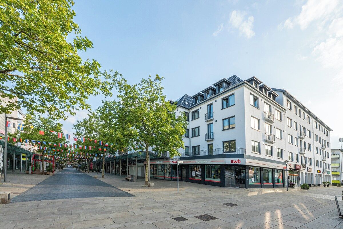 Ein modernes Gebäude mit mehreren Stockwerken, ein überdachter Außenbereich mit Geschäften und ein klarer Himmel.
