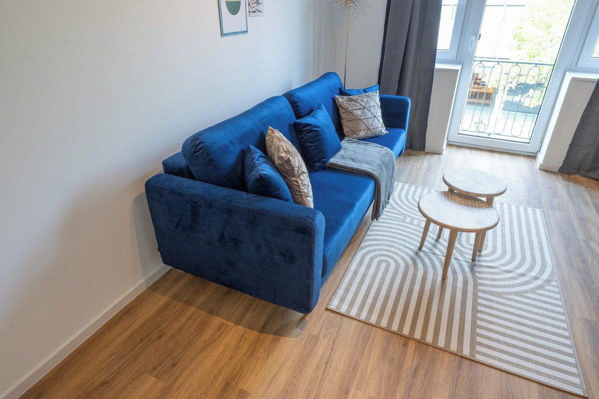 Een blauwe bank met een kamerbreed tapijt en een klein rond tafeltje in een kamer met houten vloeren en uitzicht door een glazen deur.