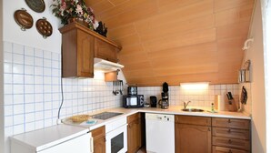 Eine kompakte Küche mit Holzschränken, einer Mikrowelle, einer Kaffeemaschine und einem Geschirrspüler.
