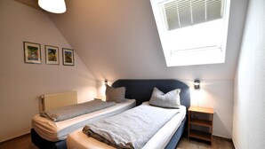 Ein Schlafzimmer mit zwei Betten, einem Oberlicht, einer Heizung und einer kleinen Holzablage.
