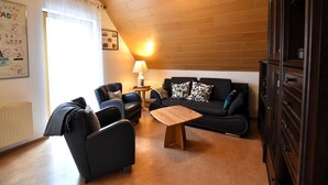Ein gemütliches Wohnzimmer mit Holzboden, einem schwarzen Sofagarnitur, einem Holztisch und einer Lampe.