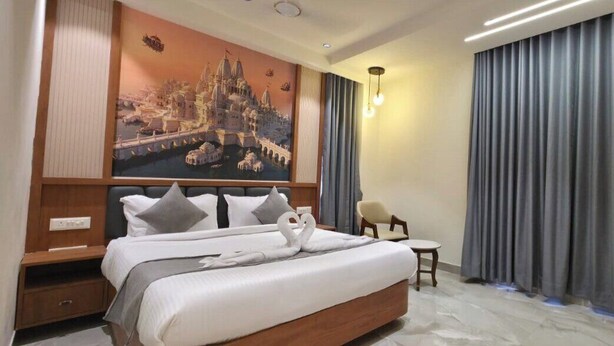 A hotel room with a large bed, a nightstand, a chair, and a painting of a cityscape. - HOTEL HANIE TREE (Dwarka)