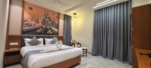 A hotel room with a large bed, a nightstand, a chair, and a painting of a cityscape. - HOTEL HANIE TREE (Dwarka)