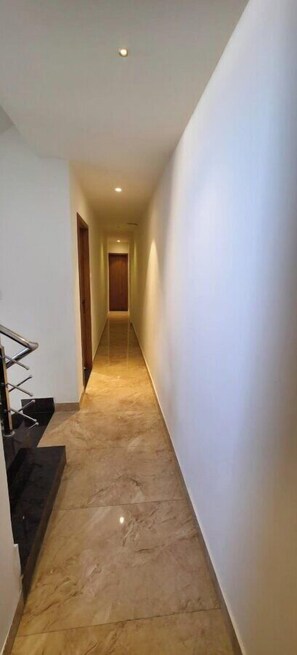 A narrow, well-lit hallway with a marble floor leading to a wooden door at the end. - HOTEL HANIE TREE (Dwarka)