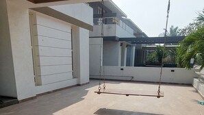 An outdoor patio area with a pergola, a swing set, and a view of a modern house in the background.