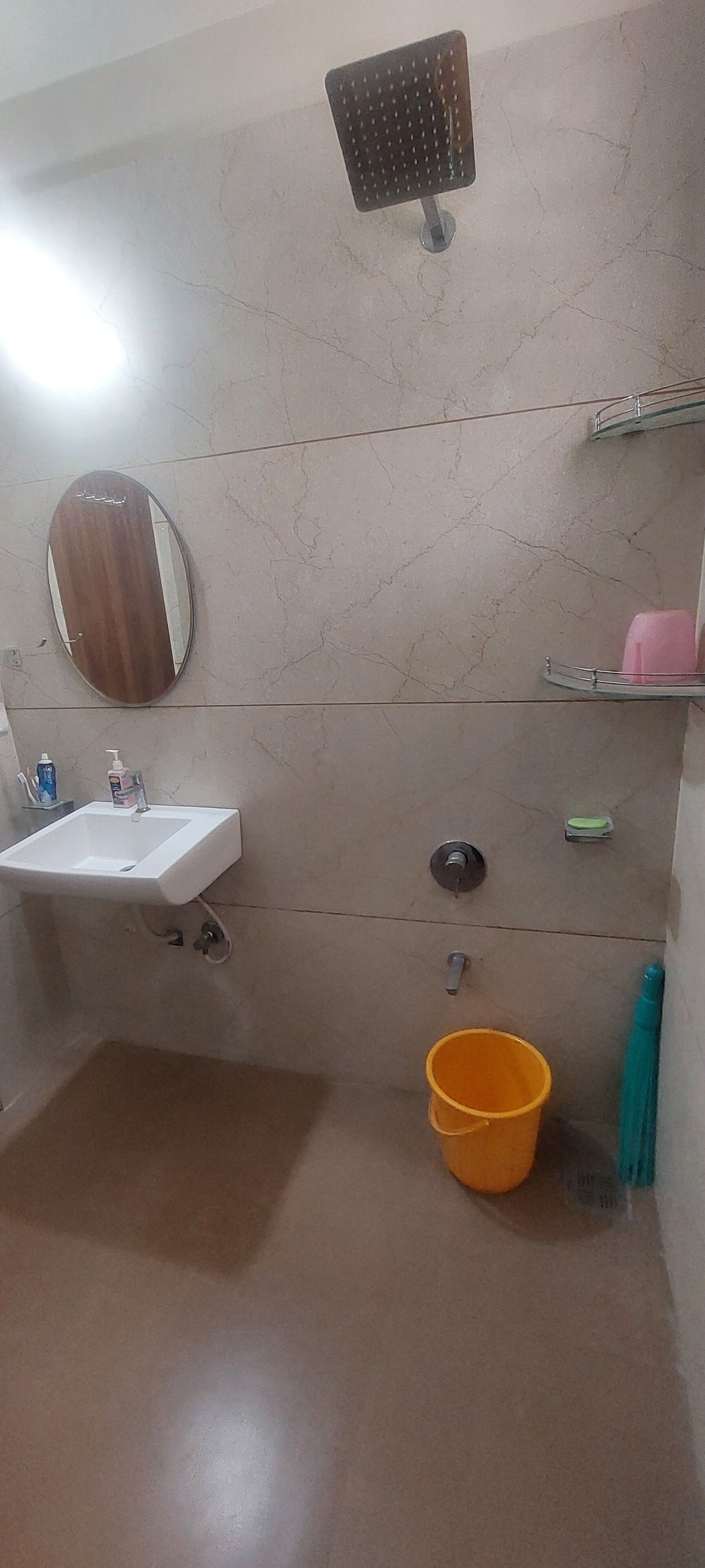 A bathroom with a sink, mirror, shower, and a yellow bucket.