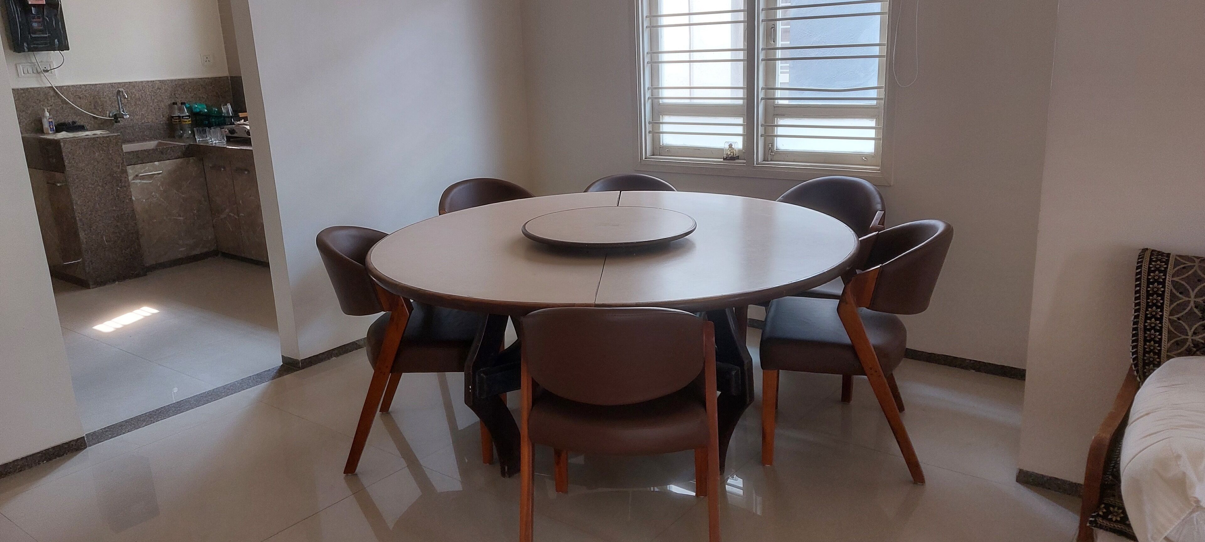 A dining area with a round table and six chairs, a kitchen with granite countertops, and a window with blinds.
