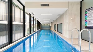 Una lunga piscina interna con corsie ben definite, ampie finestre su un lato e un cartello con informazioni sulla sicurezza a parete.