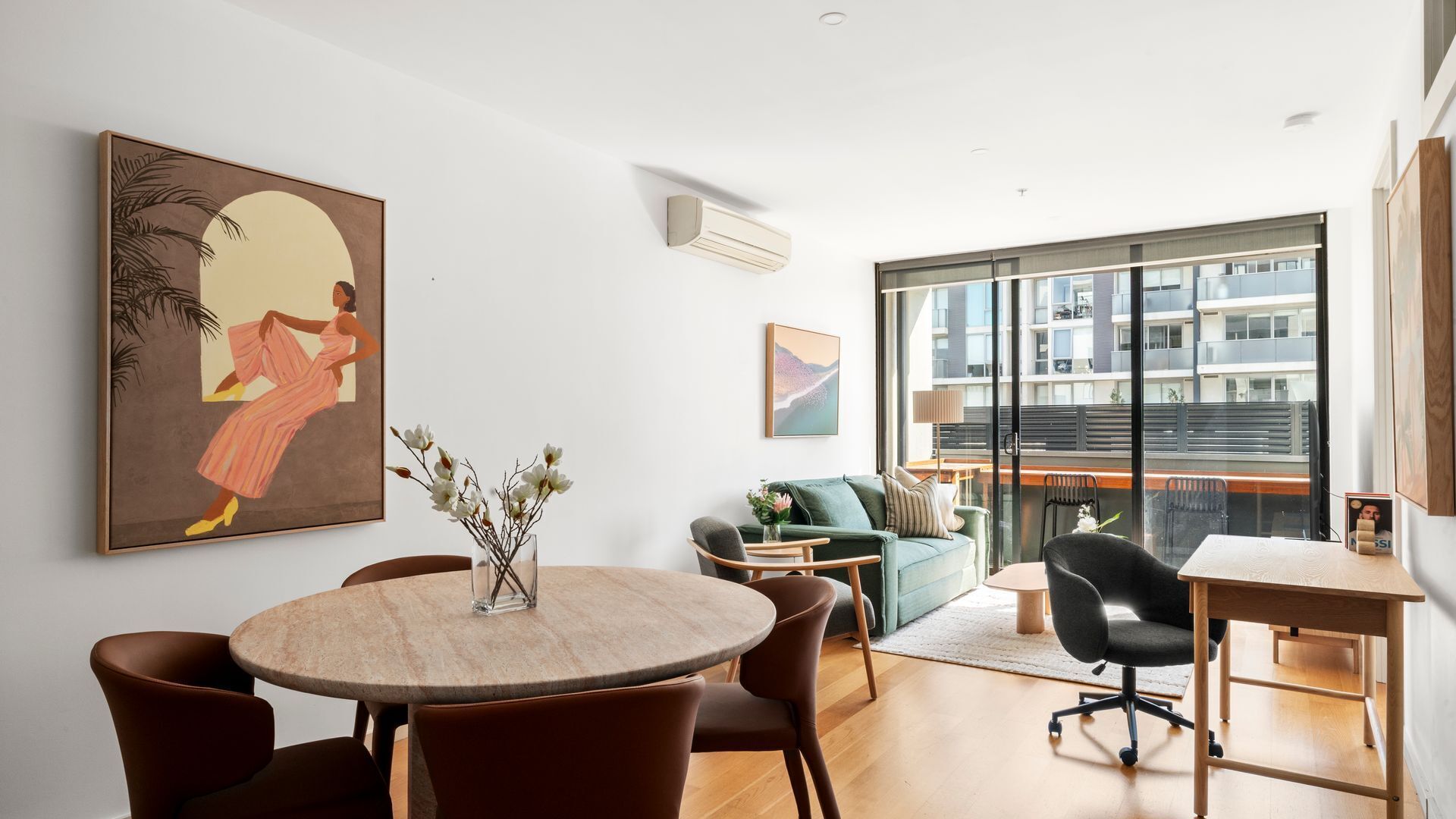 Un salón moderno con una mesa redonda de comedor, asientos cómodos, un ventanal con vistas a edificios y obras de arte en las paredes.