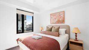 Una camera da letto con un letto, cuscini, una coperta, un comodino, una lampada e un quadro appeso al muro.
