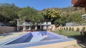 A swimming pool area with a building in the background. - Devora Resort (Rishikesh)