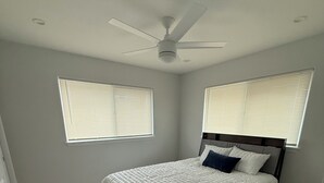 A bedroom with a bed, a ceiling fan, and two windows with blinds. - Newly built 3-bedroom house in beautiful Hilo perfect for a relaxing stay. (Hilo)