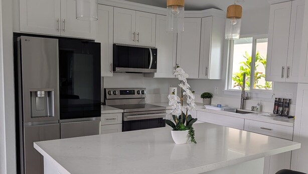 A modern kitchen with white cabinets, stainless steel appliances, and a central island with bar stools. - Newly built 3-bedroom house in beautiful Hilo perfect for a relaxing stay. (Hilo)