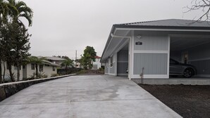 A residential driveway leading to a garage with a car parked inside. - Newly built 3-bedroom house in beautiful Hilo perfect for a relaxing stay. (Hilo)