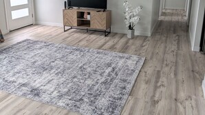 A spacious living room with a large flat-screen TV on a wooden TV stand, a grey patterned rug, and a hallway leading to another room. - Newly built 3-bedroom house in beautiful Hilo perfect for a relaxing stay. (Hilo)