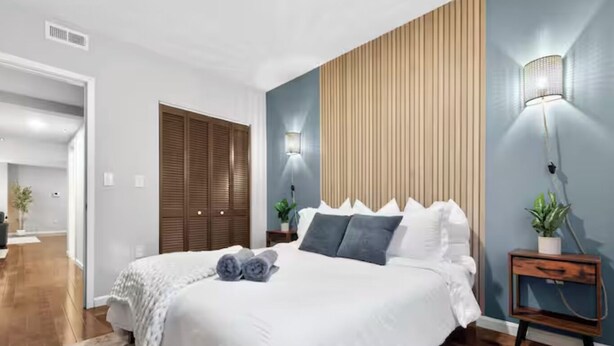 A modern bedroom with a large bed, wooden closet, and two wall-mounted lamps. - Peaceful 2-bedroom apartment - Walk Everywhere (Philadelphia)