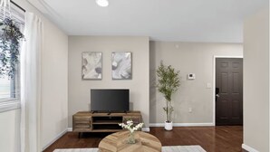 A living room with a wooden entertainment center, a flat-screen TV, a round wooden coffee table, and a potted plant. - Peaceful 2-bedroom apartment - Walk Everywhere (Philadelphia)