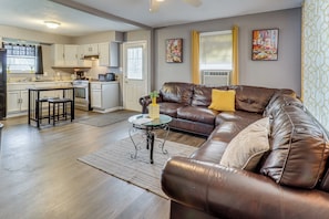 A modern kitchen with white cabinets, a dining area with a brown leather sofa, and a small round table with a vase.