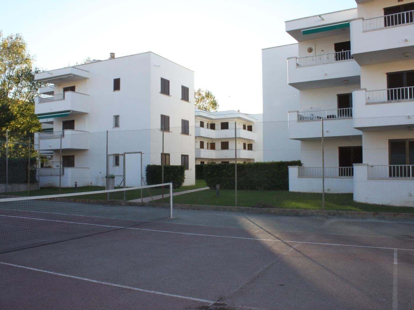 Een woongebouw met meerdere balkons, een tennisbaan en een omheind gebied.