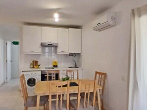 A compact kitchen with white cabinets, a built-in washing machine, and a dining area with wooden chairs and a table. - Apartment in Montgo, close to the beach. HUTG:033568-87 (l'Escala)