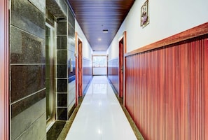 A long, narrow hallway with a polished floor, flanked by stone walls on one side and wooden paneling on the other. - GRAND HILLVIEW BY AVOOTA (Tirupati)