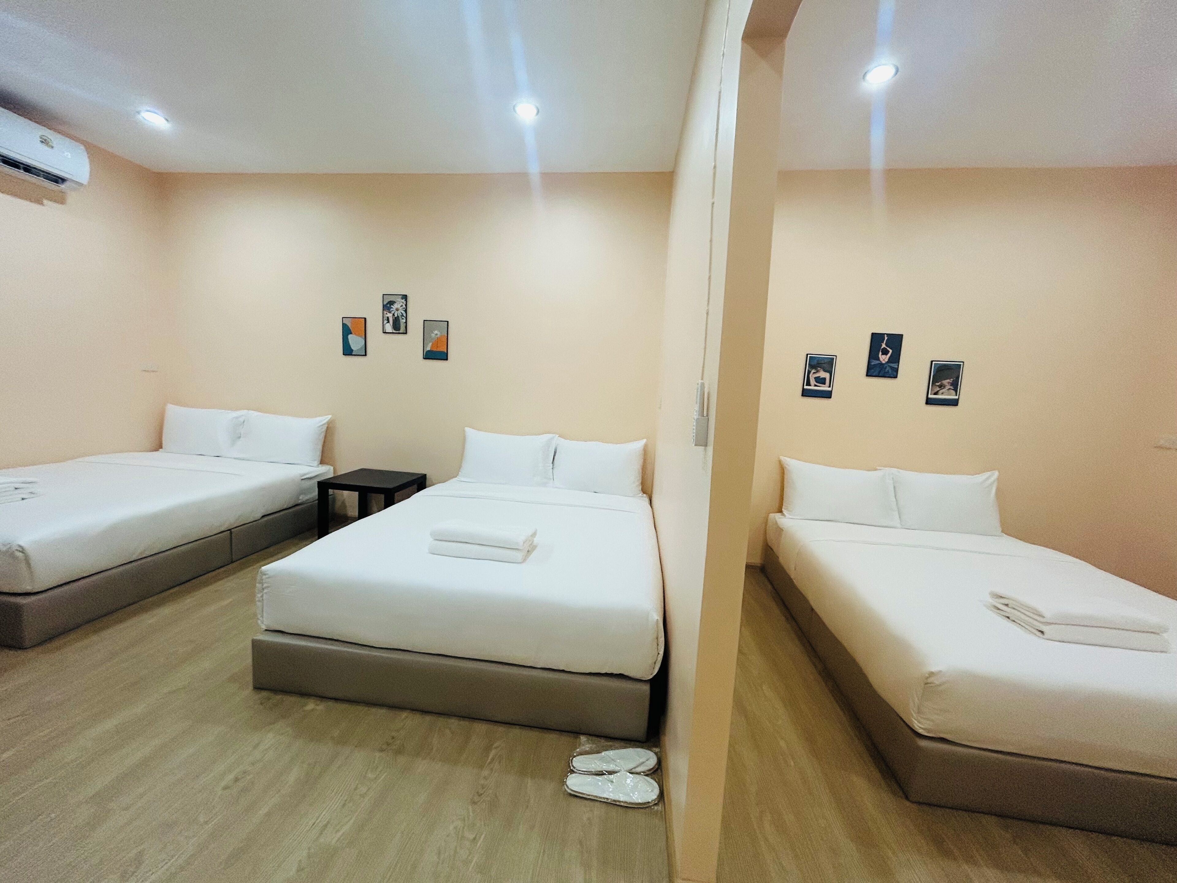 A hotel room with three beds, a small table, and a wall-mounted air conditioner.