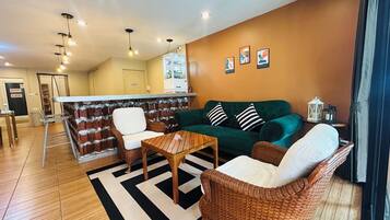 A living room with a green sofa, wicker chairs, a wooden coffee table, and a black-and-white striped rug.
