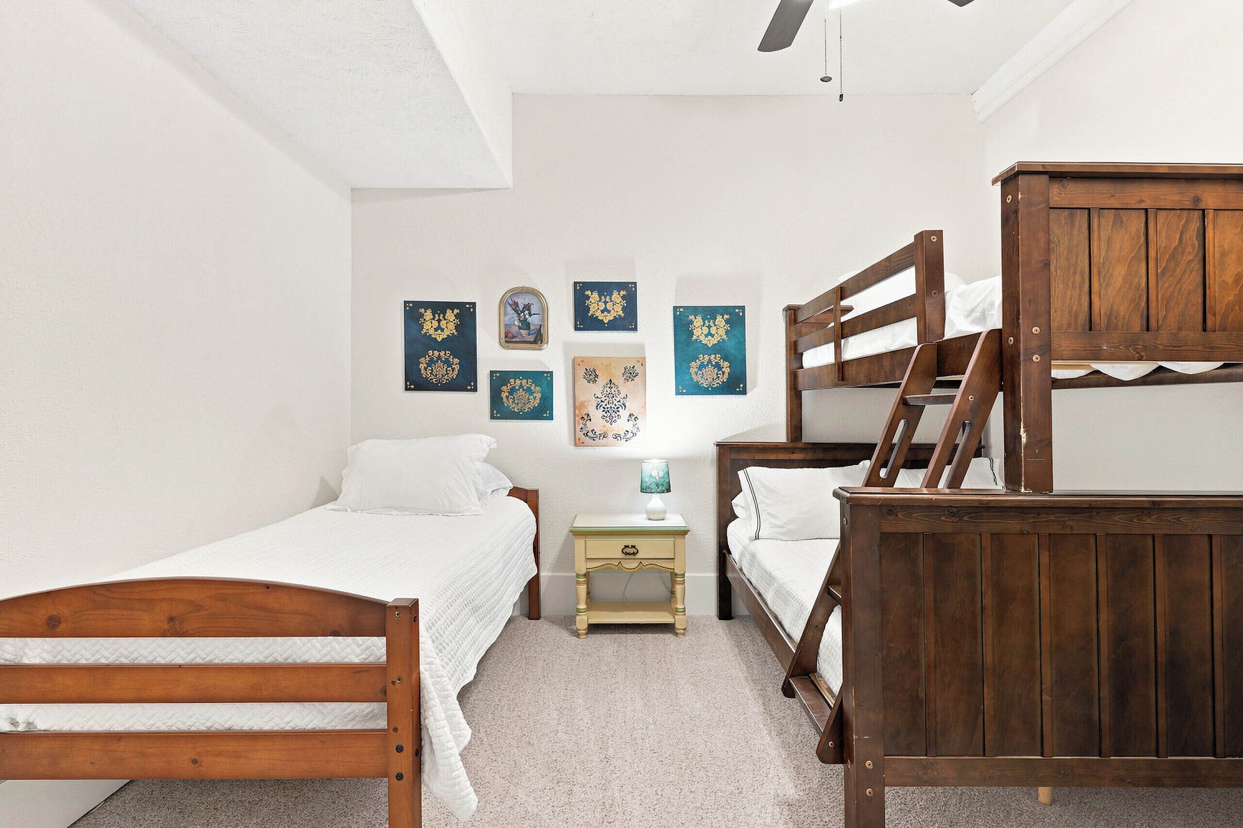 A bedroom with two wooden bunk beds, a small bedside table with a lamp, and several decorative wall pieces.