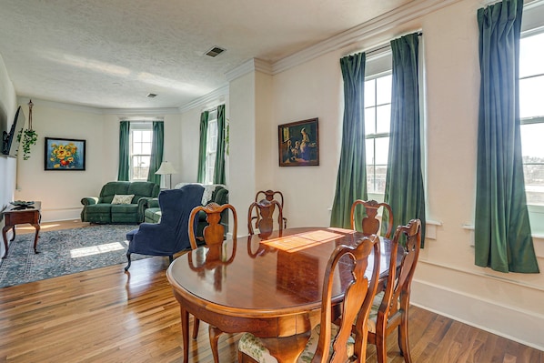 Uma sala de jantar com uma mesa e cadeiras de madeira, um sofá verde e um quadro na parede.