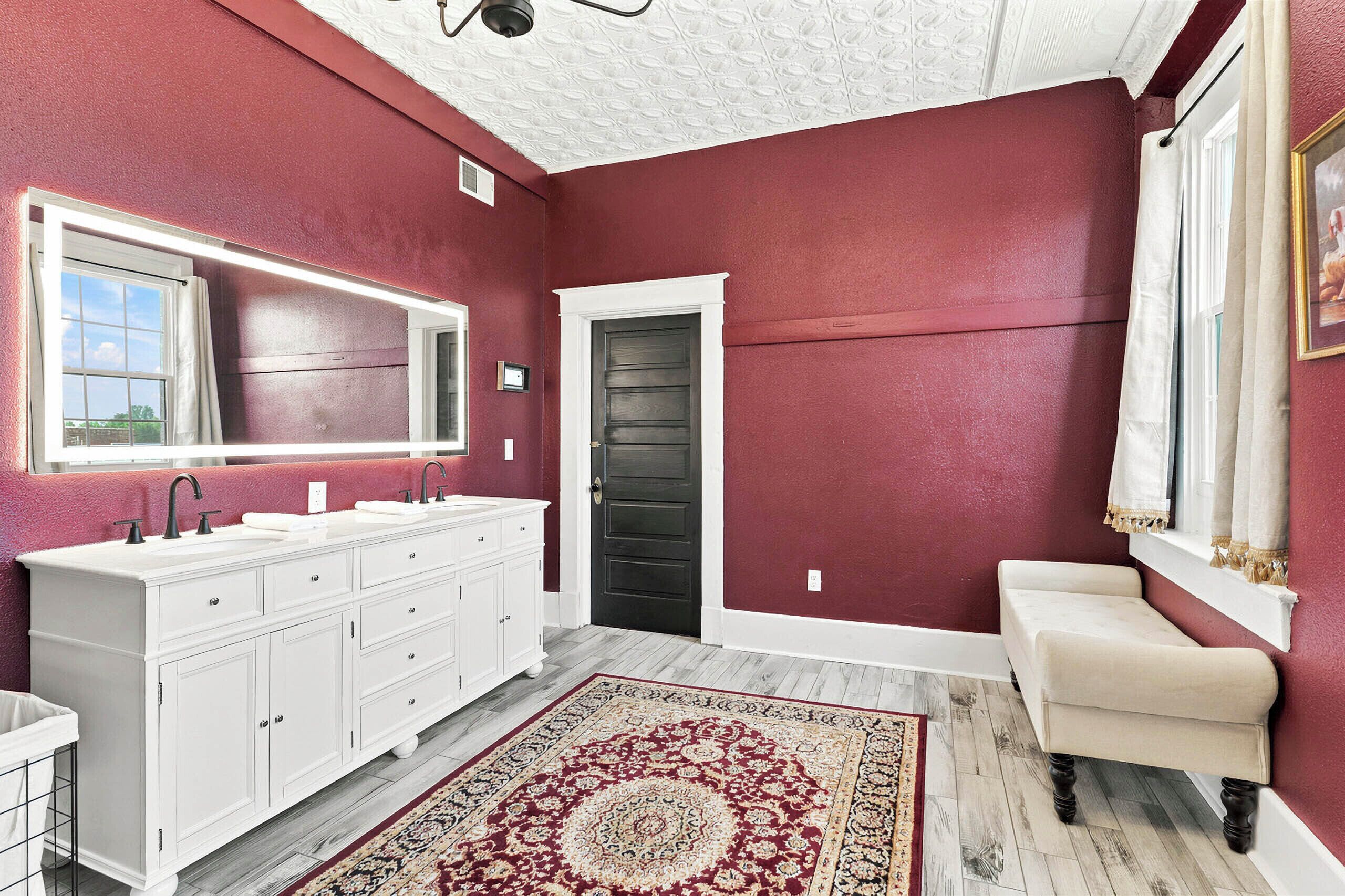Une salle de bain avec un grand meuble-lavabo, une porte sombre et un tapis à motifs.