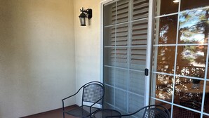 Un patio con due sedie in metallo e un tavolo, una porta bianca con una finestra e un lanterna fissata al muro.