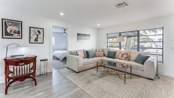 A modern living room with a sectional sofa, a wooden bench, a glass coffee table, and artwork on the walls.
