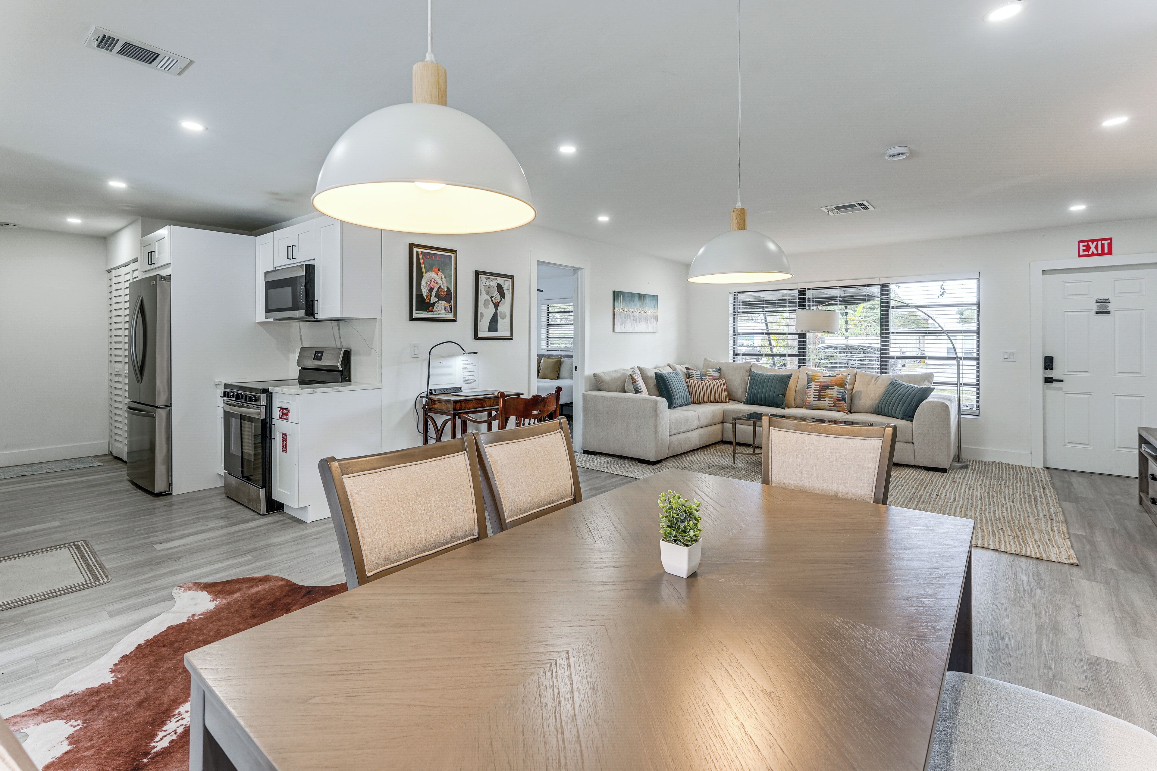 A modern kitchen with stainless steel appliances, a dining area with a wooden table and chairs, and a living room with a sofa and a television.