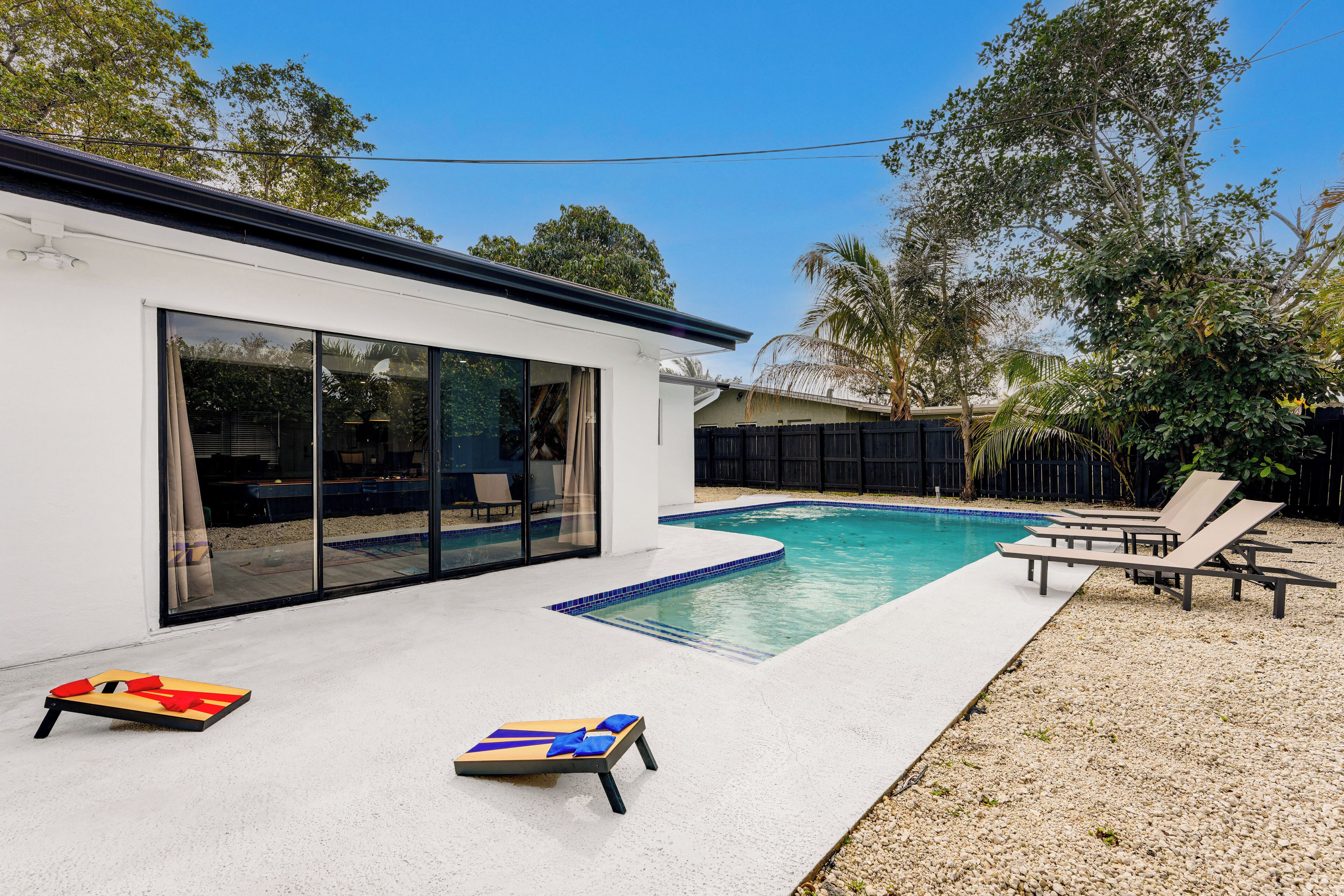 A modern house with a swimming pool, a patio with lounge chairs, and a large sliding glass door.