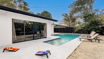 A modern house with a swimming pool, a patio with lounge chairs, and a large sliding glass door.
