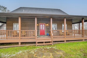 Una casa de madera con puerta roja, dos ventanas y un porche con barandillas.